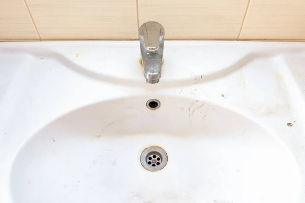 Vanha likainen pesuallas, jossa on ruostetahroja, kalkkikiveä ja saippuatahroja kylpyhuoneessa hanalla, vesihanalla — kuvapankkivalokuva