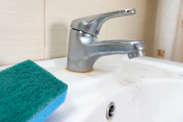 Esponja azul para lavar el grifo sucio con cal, grifo de agua calcificada con escala de cal en el lavabo en el baño, concepto de limpieza de la casa — Foto de Stock