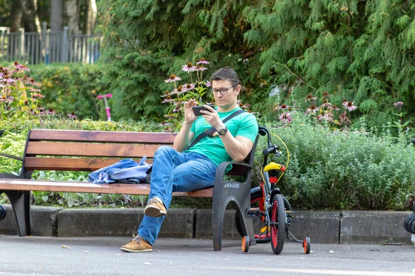 Москва, Росія - 01 вересня 2019: Людина сидить на лавці в міському парку і користується смартфоном, літній час — стокове фото