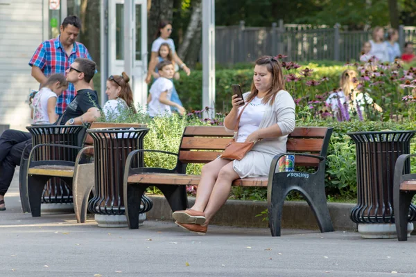 Moscú, Rusia - 01 de septiembre de 2019: Mujer sentada en el banco en el parque de la ciudad y usando un teléfono inteligente, hora de verano — Foto de Stock