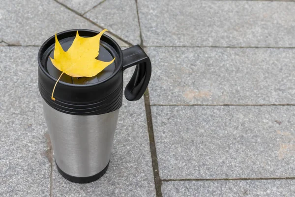 Сезон, осенние горячие напитки и концепция пикника - металлическая термокофейная чашка с красочным желтым листом на чашке с копировальным местом — стоковое фото