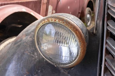 Paslı eski bir arabanın ön farları yakın.