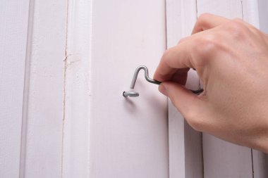 Kapı kancasını beyaz ahşap kapıya bağlayan bir el ev güvenliği ve korunma için basit bir cihaz..