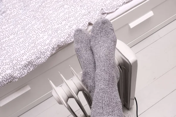 Egy nő, aki gyapjú meleg zokniban tartja a lábát egy hordozható olajmelegítőn a hideg téli vagy őszi napokon otthon. — Stock Fotó