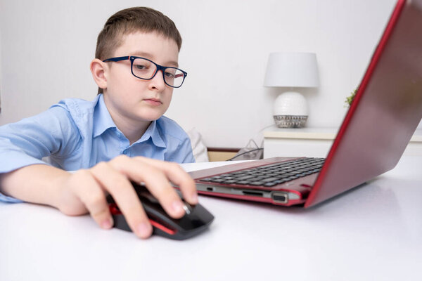 A school boy sitting by the table with a laptop and doing homework, e-learning, online education and home school concept.