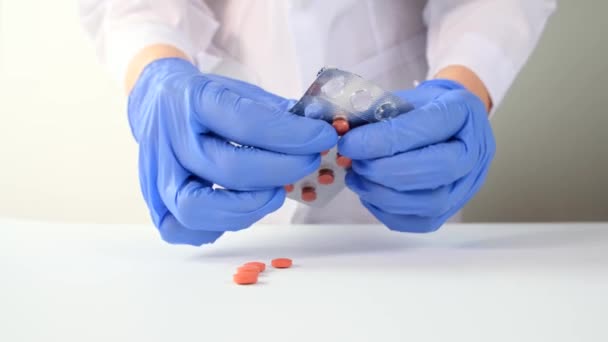 Läkare eller sjuksköterska i blå latexhandskar klämmer ut tabletter, piller ur blisterförpackningen på vitt bord närbild, sjukdomsbehandling och recept koncept — Stockvideo