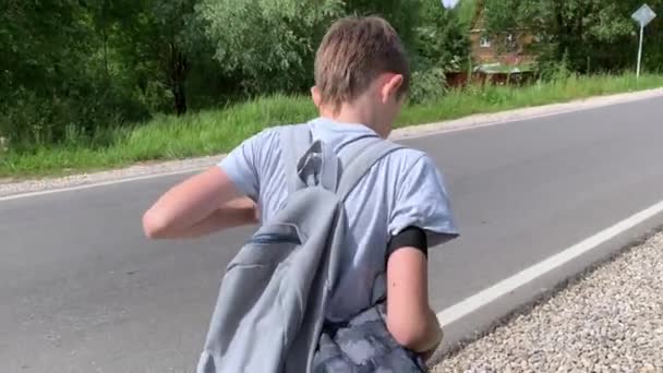 Chlapec s batohem kráčející po asfaltové cestě v létě — Stock video