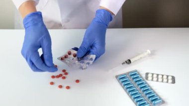 Mavi lateks eldivenli doktor veya hemşire tabletleri sıkar, beyaz masadaki su toplamasından çıkan hapları kapatır, hastalık tedavisi ve reçete konsepti, etrafta tıbbi malzemeler