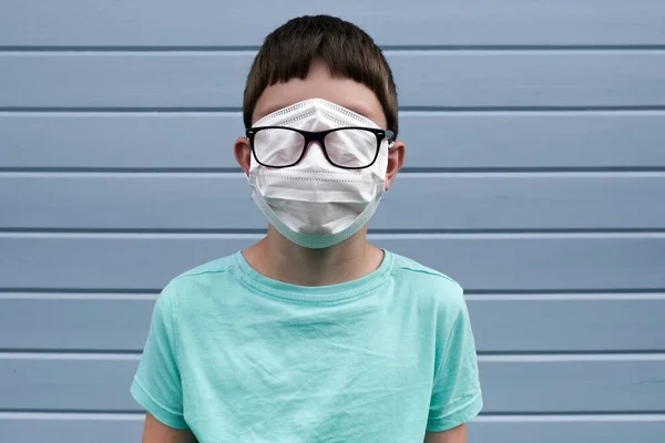 Una vista divertida de un niño con máscara médica quirúrgica protectora blanca, que cubre incluso sus ojos para prevenir la infección durante la epidemia, sus gafas sobre la máscara, broma de broma pandemia rofl —  Fotos de Stock