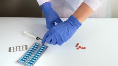 Mavi lateks eldivenli doktor veya hemşire tabletleri sıkar, beyaz masadaki su toplamasından çıkan hapları kapatır, hastalık tedavisi ve reçete konsepti, etrafta tıbbi malzemeler