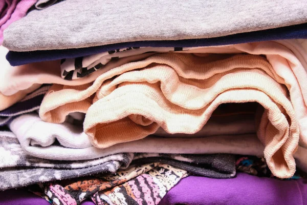 Unorganized heaps of clothes of different colors in a wardrobe lying in mess close up