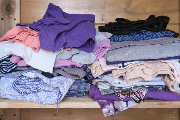 Unorganized heaps of clothes of different colors in a wardrobe lying in mess close up