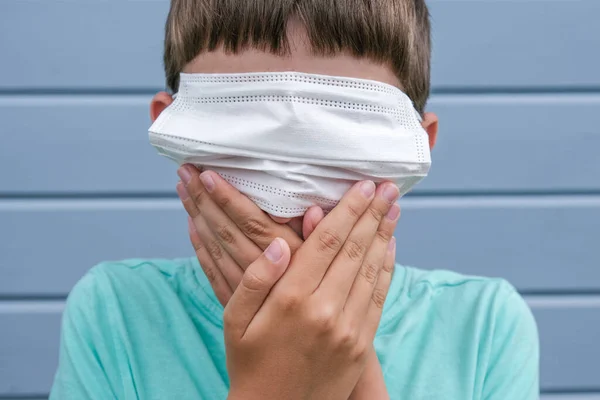 Μια αστεία άποψη ενός αγοριού που φοράει λευκή προστατευτική χειρουργική ιατρική μάσκα στα μάτια του αντί για στόμα, και καλύπτει ένα στόμα με τα χέρια, προβλήματα απόκρυψης και γεγονότα, αλισίβα για επιδημίες και πανδημία — Φωτογραφία Αρχείου