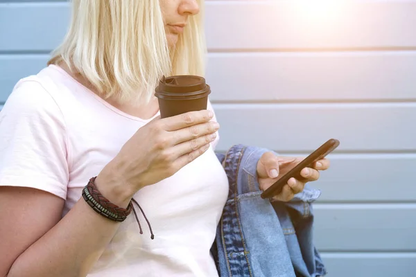 Mujer hippie con pulseras de cuero boho en una muñeca sosteniendo una taza de café para llevar y un teléfono inteligente, hora de verano — Foto de Stock