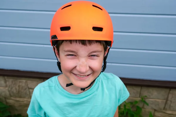 Ritratto di un adolescente caucasico felice e sorridente che indossa un casco da incidente sportivo arancione, impara ad andare in bicicletta o skateboard in estate, sicurezza e protezione mentre i bambini all'aperto fanno attività — Foto Stock