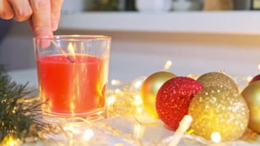 Kırmızı bir Noel mumu, Noel çelengi, çam ağacı süslemeleri ve topları olan bir masada yanan bir mum.