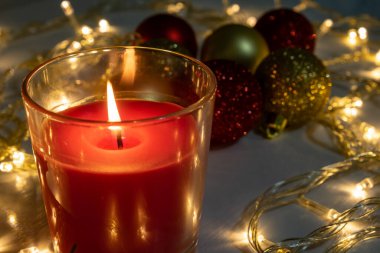 Kırmızı Noel mumu, yanan mum ateşi Noel çelengi, çam ağacı süslemeleri ve topları olan bir masada.