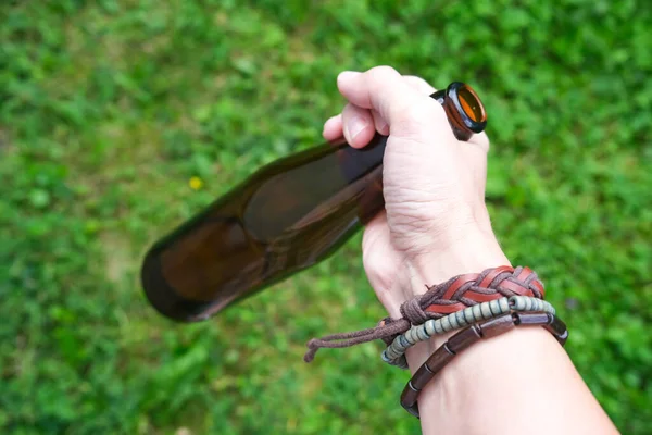 Una mano de un hippie, hipster sosteniendo una botella de alcohol, cerveza. Jóvenes con concepto de adicción al alcohol. Alegría veraniega y picnic — Foto de Stock