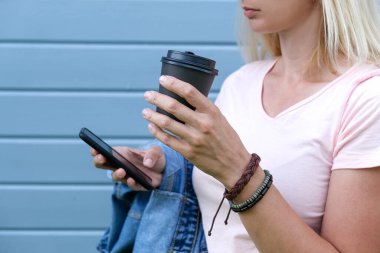 Bileğine deri bileklikler takan hippi bir kadın. Elinde bir fincan kahve ve bir akıllı telefon var.