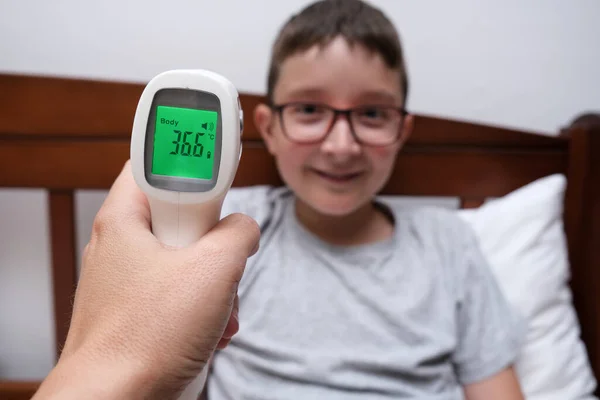 Egy boldog mosolygós fiú normál hőmérséklettel, amely megjelenik az infravörös érintésmentes hőmérő kijelzőjén, koncepció pf egészséges gyermek — Stock Fotó