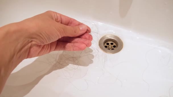 Ένα χέρι συλλογής σκούρα μακριά γυναικεία πεσμένα μαλλιά σε ένα μπολ πλύσης, τριχόπτωση μετά το πλύσιμο και το βούρτσισμα των μαλλιών, ανδρογόνο αλωπεκία — Αρχείο Βίντεο