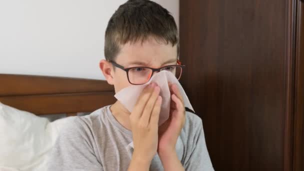 Un ragazzo con influenza e febbre sdraiato a letto e soffiato il naso con un fazzoletto di carta, concetto di malattie virali stagionali — Video Stock