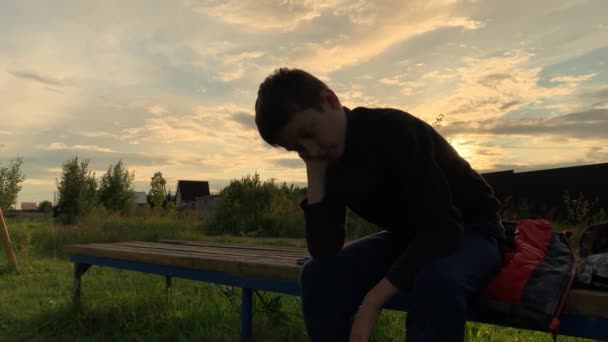 A lonely sad boy sitting outdoors on a bench at sunset, unhappy depressed child with discrimination and bullying problems — Stock Video