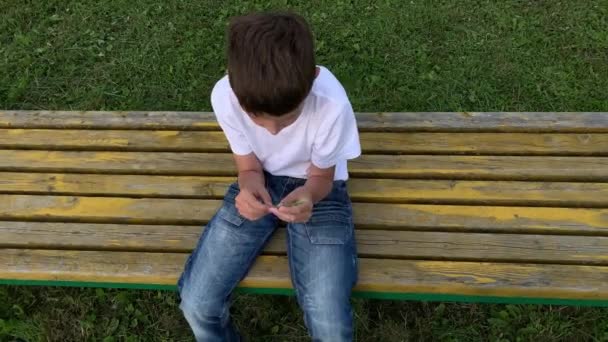 A lonely sad boy sitting outdoors on a bench, unhappy depressed child with discrimination and bullying problems, top view — Stock Video