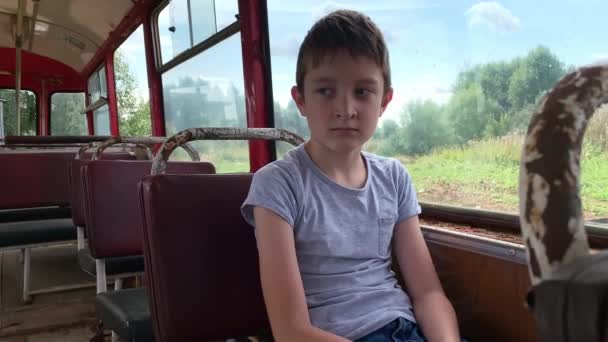 A 10 years boy riding in a old vintage bus, he is sad because his poor life and the bus moving going on a dirty country road — Stock Video