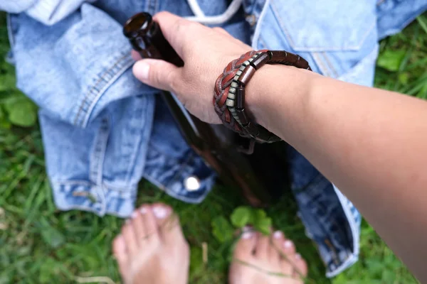 Una mano de un hippie, hipster sosteniendo una botella de alcohol, cerveza. Jóvenes con concepto de adicción al alcohol. Alegría veraniega y picnic —  Fotos de Stock