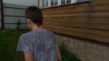 Şiddetli yağmur altında genç bir çocuk eve yürüyor, hava kötü ve giysileri ıslak. Kırsalda gri bulutlu bir gökyüzü ve fırtına