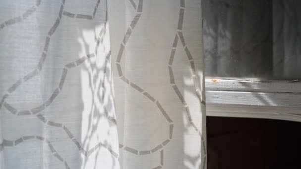 A light transparent curtain gently moving by the wind on sunny summer day, countryside. Sun rays falling on a textile and making fancy romantic shadows, early morning atmosphere — Stock Video