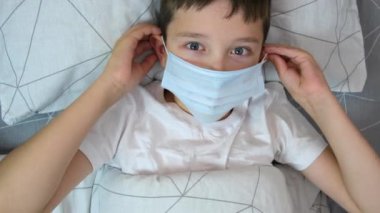 Hasta beyaz bir çocuğun portresi. Yatakta yatıyor ve koruyucu bir maske takıyor. Hastalık ve grip konsepti.