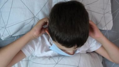 Hasta beyaz bir çocuğun portresi. Yatakta yatıyor ve koruyucu bir maske takıyor. Hastalık ve grip konsepti.