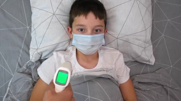 赤外線非接触温度計のディスプレイに表示されている正常な温度の回復中の少年 コンセプトPf健康的な子供 彼女の息子の母親の温度を測定 — ストック動画