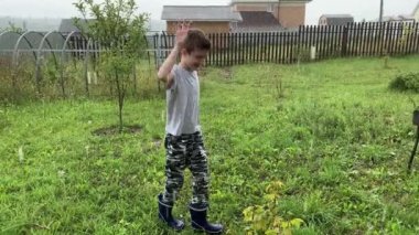 Sağanak yağmurun altında durup yağmur damlalarını, sağanakları ve kötü havayı yakalayan mutlu bir çocuk.