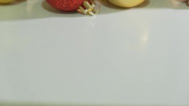 Kırmızı ve altın noel topları simle süslenmiş. Beyaz masaya yakın ve arka planda bir çelenkle süslenmiş.