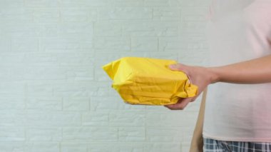 Sarı, turuncu bir paket taşıyan bir kadın onu başka birine veriyor.