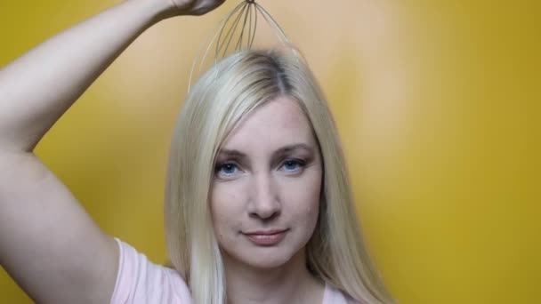 Une femme blonde caucasienne profiter d'un massage du cuir chevelu de la tête par un outil anti stress acupuncture pieuvre métallique, équipement, elle ferme les yeux avec plaisir, fond jaune — Video