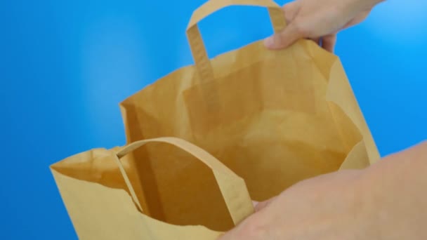 Mãos abrindo e mostrando saco de compras de papel contra fundo azul, usando sacos recicláveis para compras para salvar a natureza, proteção ambiental — Vídeo de Stock