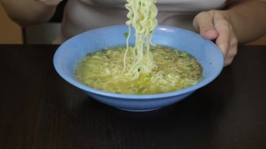 Masada oturan bir kadın seramik tabaktan çatalla hazır yumurtalı erişte yiyor.