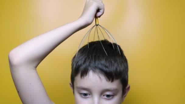 Un băiat caucazian se bucură de masajul scalpului capului prin acupunctura anti stres instrument de caracatiță metalică, echipamente, închide ochii cu plăcere, fundal galben, vedere de aproape — Videoclip de stoc