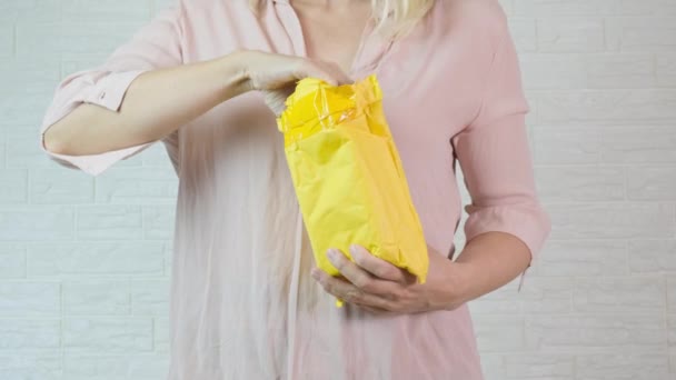 En kvinna packar upp, packa upp ett orange gult paket och tar ut innehåll — Stockvideo