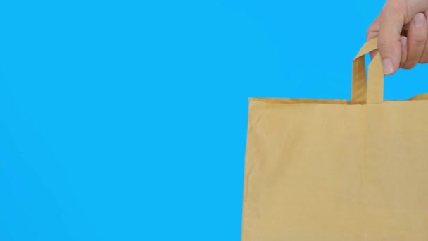 Sebuah kantong belanja kertas berlatar belakang biru, menggunakan tas daur ulang untuk pembelian demi menyelamatkan alam, perlindungan lingkungan — Stok Video