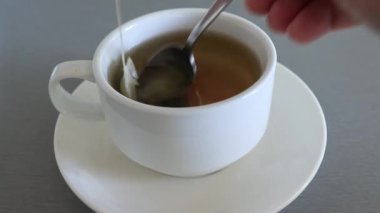 Sabahları mutfakta beyaz bir seramik fincanda çay poşeti demleyen eller kahvaltıda taze bitki çayı yakın.