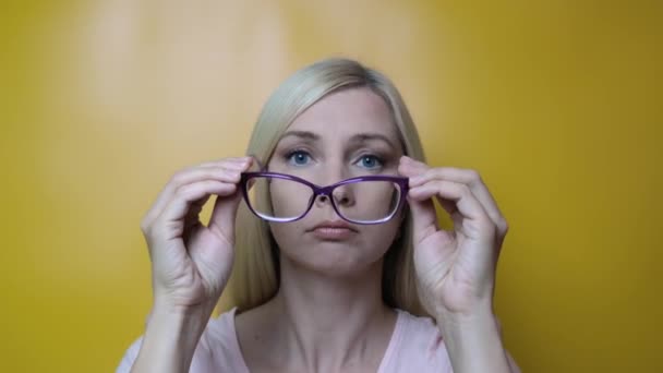 A middle age blond woman putting on stylish fashionable glasses and smiling to camera against yellow background, myopia, astigmatism and ophthalmologic diseases comcept — Stock Video