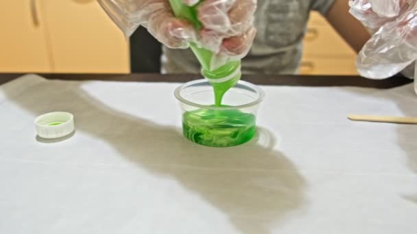 Ein Junge, der zu Hause grünen Schleim herstellt, DIY-Projekt, Chemie-Experiment, er gießt die Zutaten in einen Behälter und mischt sie — Stockvideo