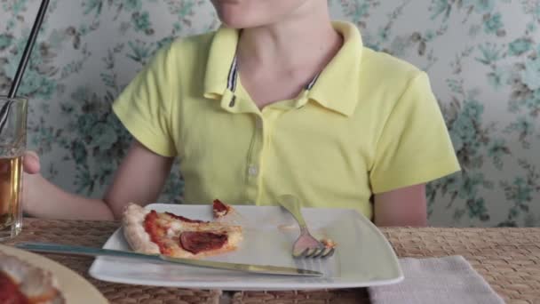 Um menino comendo pizza em um restaurante e bebendo suco de maçã de um copo através de uma palha — Vídeo de Stock