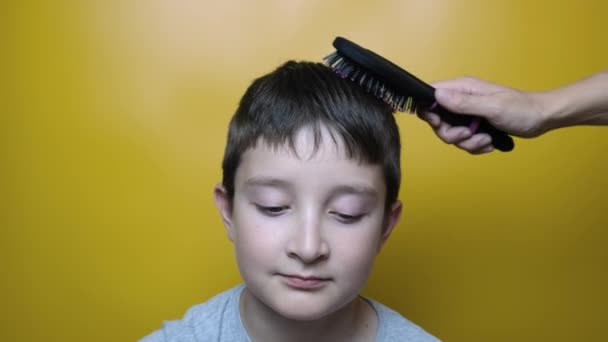 Une mère d'un coiffeur peignage, brossant les cheveux d'un garçon sur fond jaune — Video