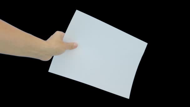 En hand som håller ett vitt tomt papper A4 med kopieringsutrymme mot svart bakgrund — Stockvideo